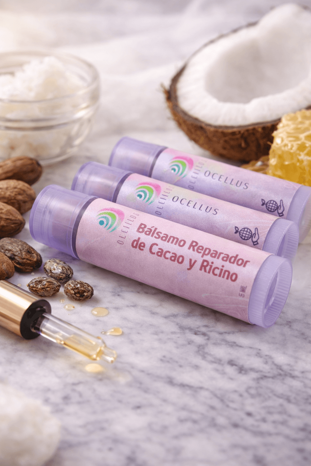 Bálsamos labiales Ocellus de cacao y ricino con coco, miel y semillas sobre mármol.
